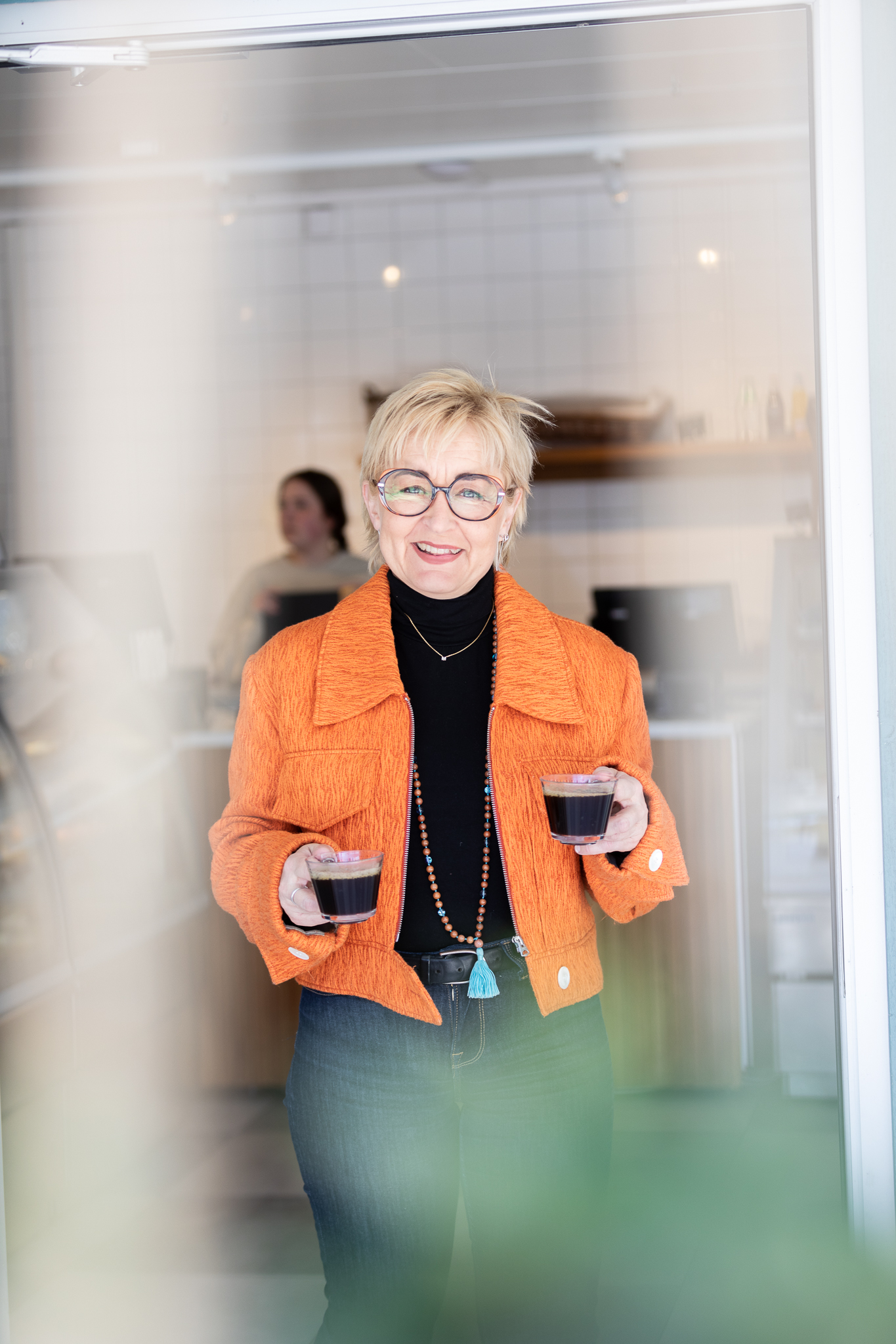 Maria Åberg i dörröppningen med två koppar kaffe