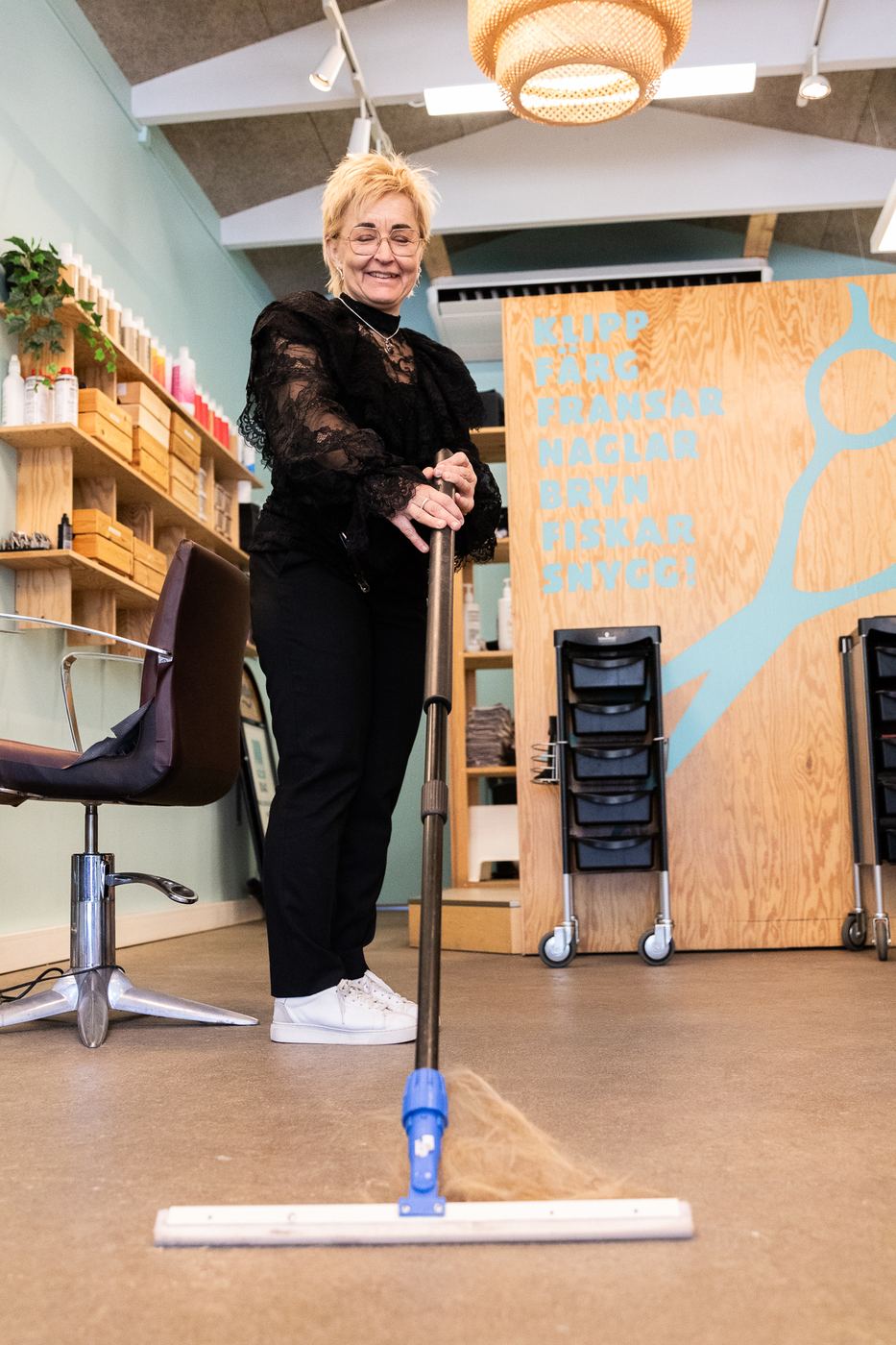Maria Åberg sopar hår i salongen och skrattar