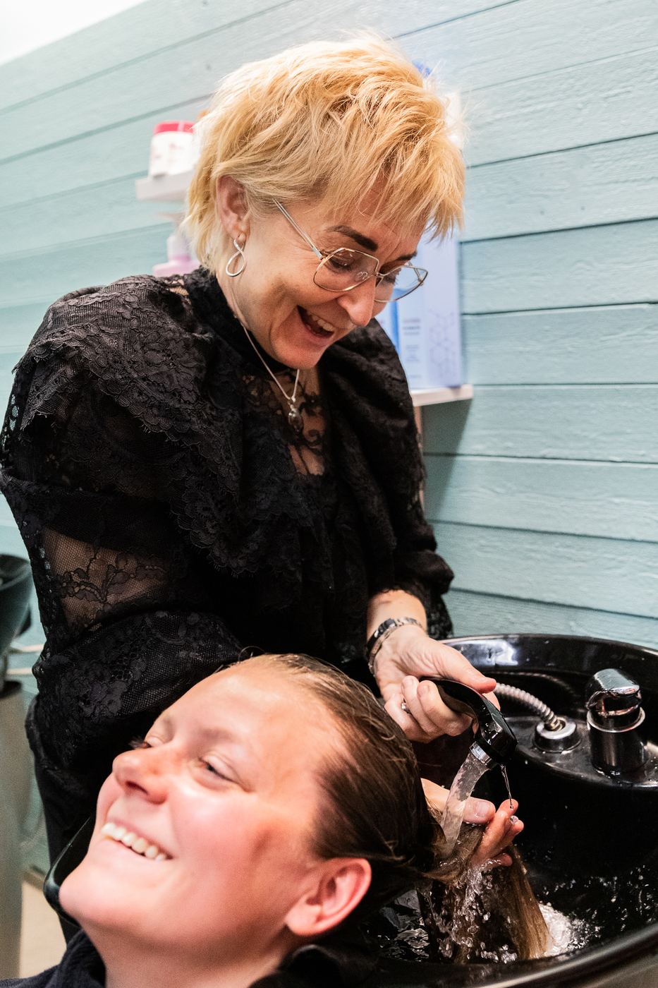 Maria Åberg sköljer en kunds hår, båda skrattar